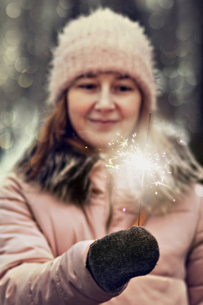 Рождественские огни яркие брызги, жгущие в руках расплывчатой счастливой женщины в парке. Спарклер. Emotions, New Year 's mood.Winter holidays. - Фото, изображение