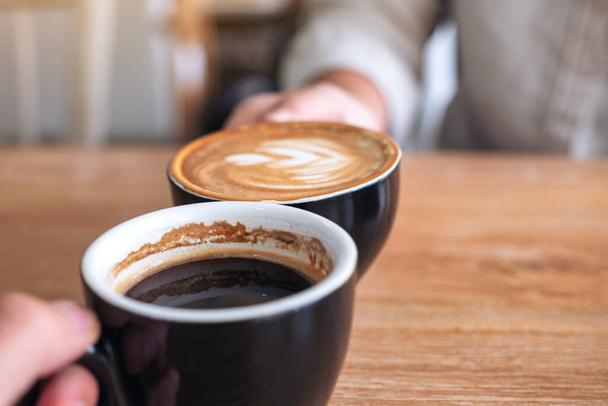 Kafe 'de iki kahve fincanını ahşap masaya tokuşturan bir adam ve bir kadının yakın görüntüsü. - Fotoğraf, Görsel