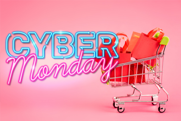red paper bags in small shopping trolley near cyber monday lettering on pink - Photo, Image