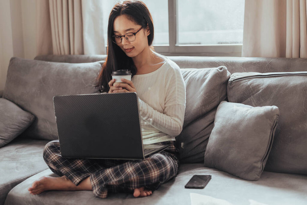 Young woman working on laptop and drinking coffee at home. Beautiful busineeswoman working at home and take a break. Working at home during Coronavirus or Covid-19 quarantine. - Photo, Image