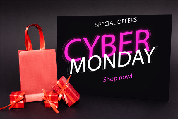 red presents and shopping bag near placard with special offers, cyber monday, shop now lettering on dark background - Fotó, kép