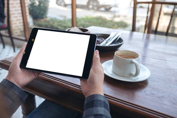 Mockup image of woman's hands holding black tablet pc with blank screen horizontally with coffee cup on wooden table in cafe - Photo, Image