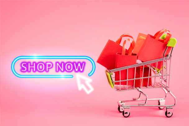 shopping bags in small trolley near shop now lettering on pink, black friday concept - Photo, Image