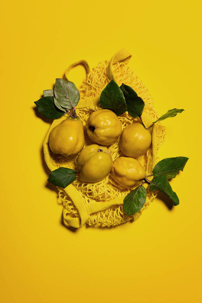 黄色の背景に黄色のメッシュバッグにいくつかの豪華なリンゴ。ビューの真上。果物や葉には自然な欠陥、斑点、傷があります。環境に優しいショッピングと持続可能な生活の概念 - 写真・画像