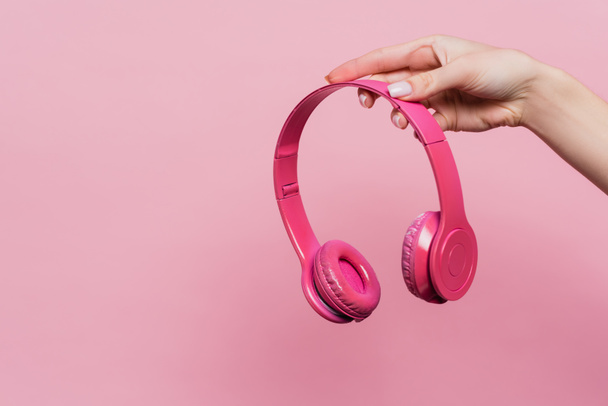 částečný pohled na ženu držící bezdrátová sluchátka izolovaná na růžové - Fotografie, Obrázek