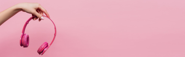 partial view of woman holding wireless headphones isolated on pink, banner - Photo, image