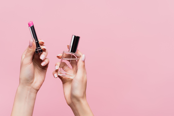 bijgesneden beeld van vrouw met lippenstift en fles met parfum geïsoleerd op roze - Foto, afbeelding