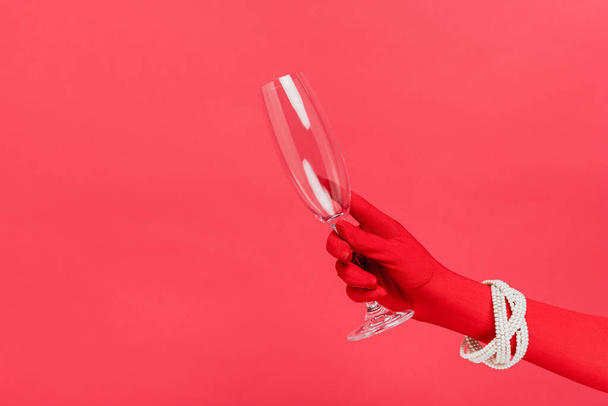 vista recortada de la mujer en guante sosteniendo la copa de champán vacío aislado en rojo - Foto, imagen