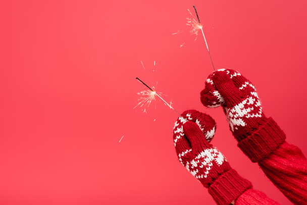 cropped view of woman in mittens holding sparklers isolated on red - Photo, Image