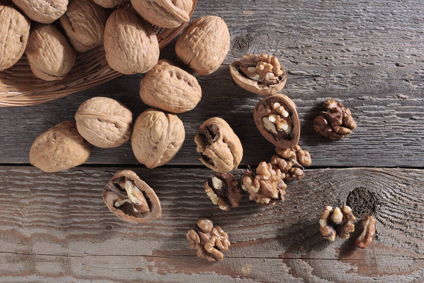 Whole and cracked walnuts on old wooden background, top view - Foto, afbeelding