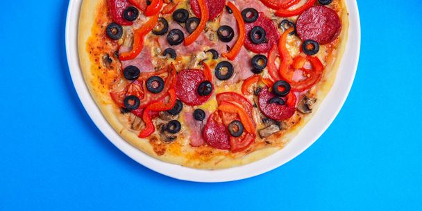 A whole, cooked and sliced peperoni pizza on a colorful backgroud, various colors. Copy space banner. Italian cuisine concept, fast food, junk food. - Foto, afbeelding