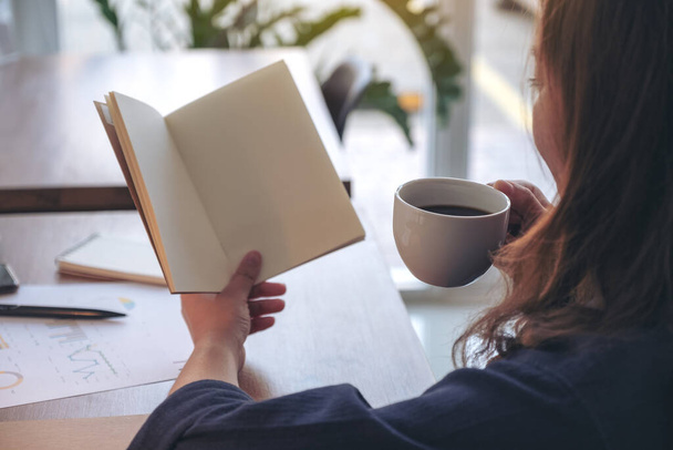 Immagine ravvicinata di una donna che tiene in mano e apre un quaderno bianco mentre beve caffè - Foto, immagini