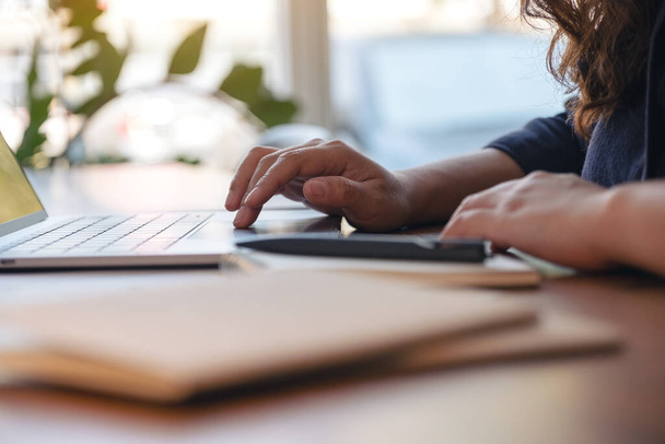 Imagem de perto da mão de uma mulher usando e tocando no touchpad do laptop com cadernos e papéis na mesa no escritório - Foto, Imagem
