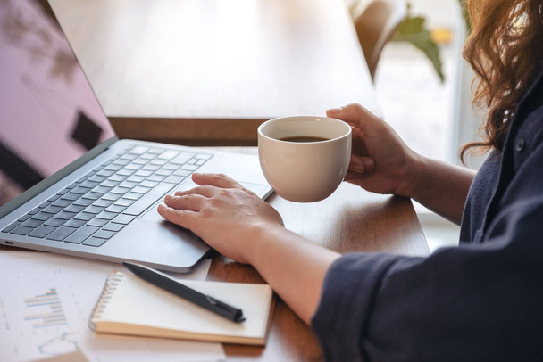 Close-up beeld van een vrouw aanraken op laptop touchpad tijdens het drinken van koffie en het werken in het kantoor - Foto, afbeelding