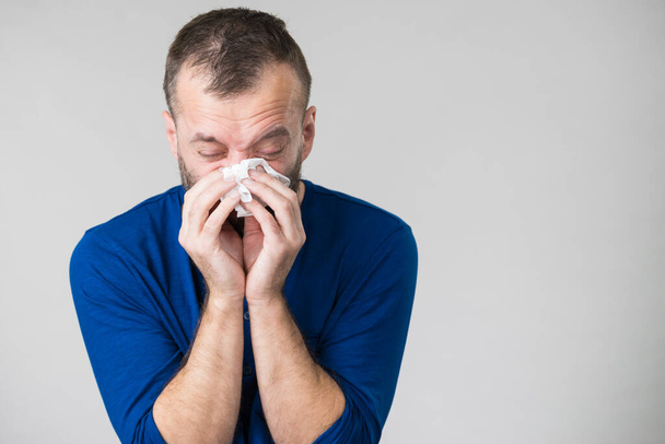 Ο άνθρωπος που έχει γρίπη, φταρνίζεται στον υγιεινό ιστό. Ο τύπος είναι άρρωστος, αλλεργικός φυσάει τη μύτη του. - Φωτογραφία, εικόνα