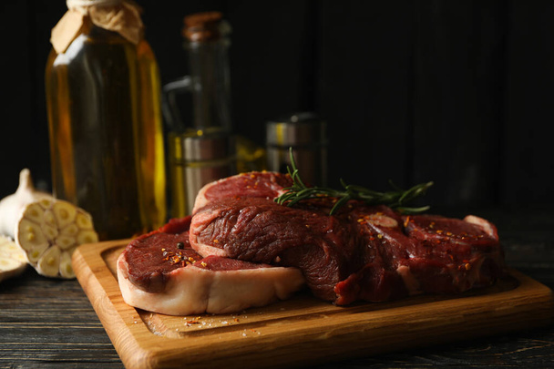 Épices, huile et carton avec viande de steak crue sur fond en bois - Photo, image