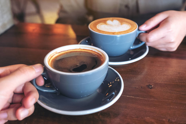 Close up image of a man and a woman clinking blue coffee mugs on wooden table in cafe - Photo, Image