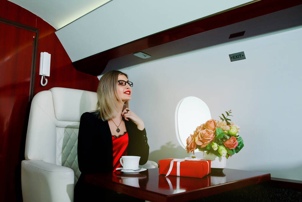 Cute young businesswoman with gift flying in luxury private jet. Business woman in airplane first class seat during trip. Concept quality of passenger service in aviation industry, travel at highest - Foto, Imagem