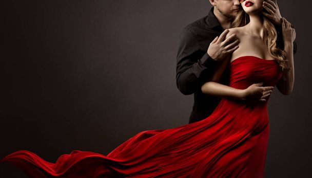 Romantic Lovers Couple Dancing. Man hugging and kissing beautiful Woman in Silk Red flying Dress. Fashion Portrait. Studio Black Background - Zdjęcie, obraz