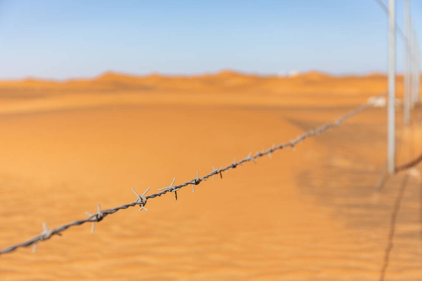 Alambre de púas simple con dunas desérticas en el fondo en la aldea fantasma Al Madam, Emiratos Árabes Unidos. - Foto, Imagen