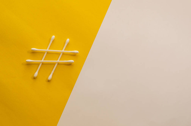 hisopos de algodón en forma de signo de hashtag sobre fondo blanco y amarillo. Fondo conceptual minimalista con espacio de copia. - Foto, imagen