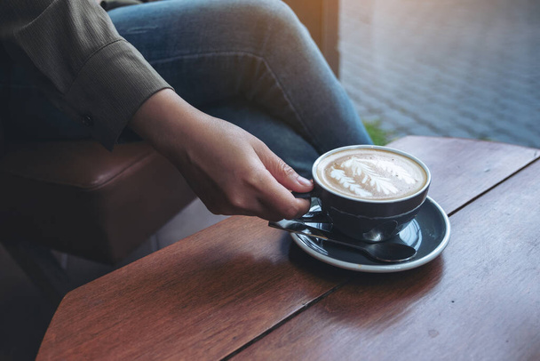 Imagen de cerca de la mano de una mujer sosteniendo y bebiendo café con leche caliente mientras está sentada en la cafetería - Foto, imagen