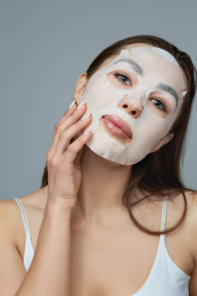 Beauty face skin care. Woman apply a cloth moisturizing mask on face . Girl model with cosmetic mask. Facial  treatment - Fotoğraf, Görsel