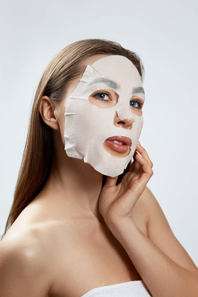 Face care and beauty treatments. Woman with a cloth moisturizing mask .Cosmetic procedure. spa and cosmetology. - 写真・画像