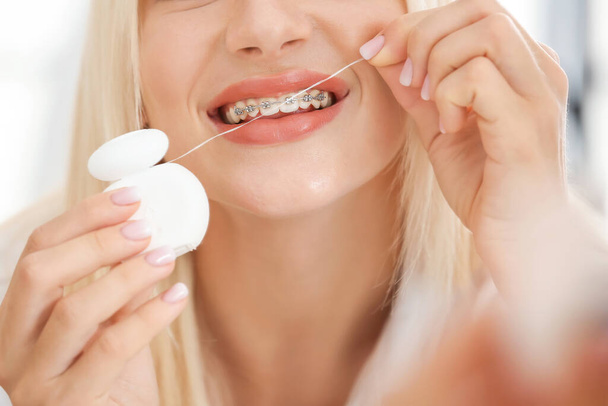 Νεαρή γυναίκα με οδοντικά σιδεράκια και οδοντικό νήμα, κοντινό πλάνο - Φωτογραφία, εικόνα