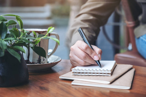 Nahaufnahme der Handschrift einer Frau auf leerem Notizbuch mit Kaffeetasse auf Holztisch - Foto, Bild