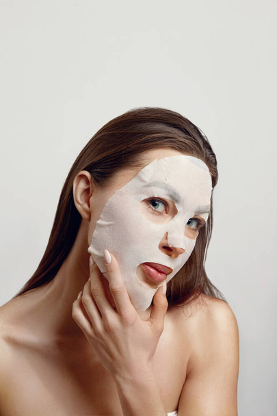 Beautiful Young Woman with facial mask looking at camera. Cosmetic procedure. Girl Beauty spa - Photo, image