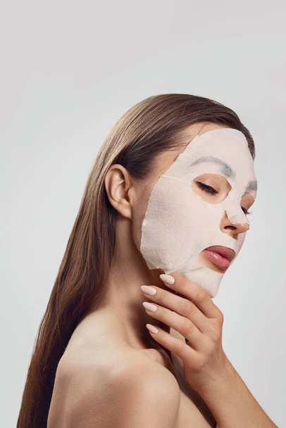 Beautiful woman with a cloth moisturizing  mask for the face. Facial and Spa treatment . Cosmetic mask. - Foto, Imagem