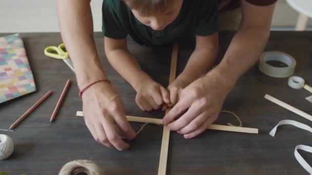 Top-view close-up van onherkenbare handen van vader en zoon wikkelkoord rond houten frame voor het vervaardigen van handgemaakte vlieger - Video