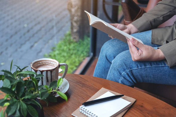 Nahaufnahme einer Frau beim Öffnen eines Buches mit Notizbüchern und Kaffeetasse auf einem Holztisch im Café  - Foto, Bild