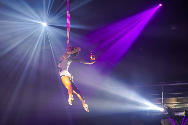 Mujer joven flexible hacer rendimiento en correas aéreas, flexible de nuevo en correas aéreas, espectáculo de circo aéreo, luz blanca púrpura. Mujer flexible gimnasta en correas - Foto, Imagen