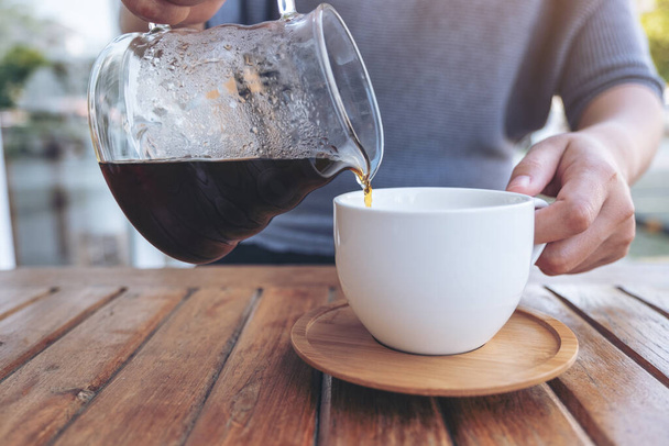Closeup image of a hand pouring drip coffee into a white mug on vintage wooden table - Valokuva, kuva
