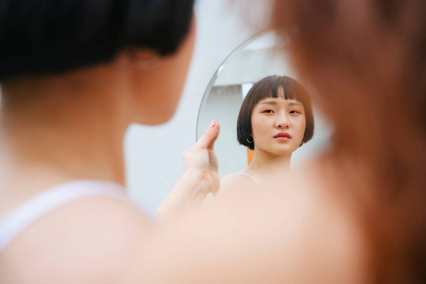 Ασιάτισσα νεαρή κοντή γυναίκα χτένισμα κοιτάζοντας στον καθρέφτη. - Φωτογραφία, εικόνα