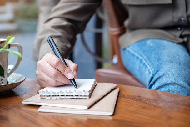 Közelkép egy nő kézírásáról üres jegyzetfüzetre, kávéscsészével a fa asztalon. - Fotó, kép