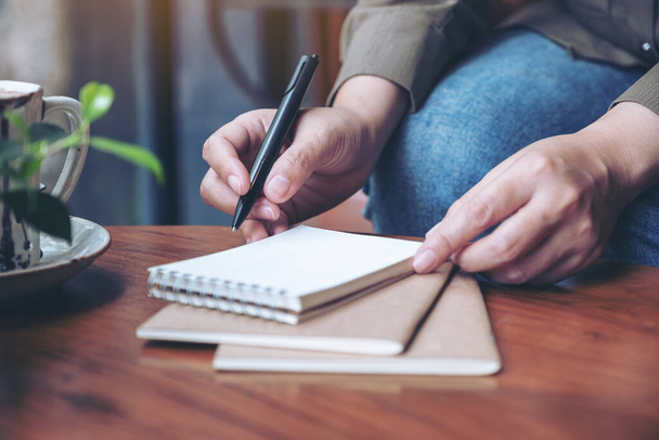 木製のテーブルの上にコーヒーカップで空白のノートに書く準備をしている女性の手のクローズアップイメージ - 写真・画像