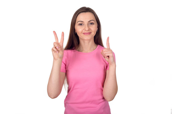 Szczęśliwa młoda dziewczyna w różowej kurtce pokazuje dwa palce znak V, izolowane na białym tle. - Zdjęcie, obraz