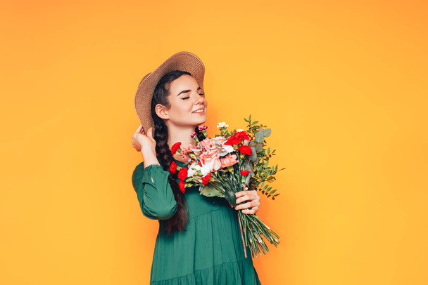 Woman holding a large bouquet of flowers in a green dress on a yellow background. - Photo, Image