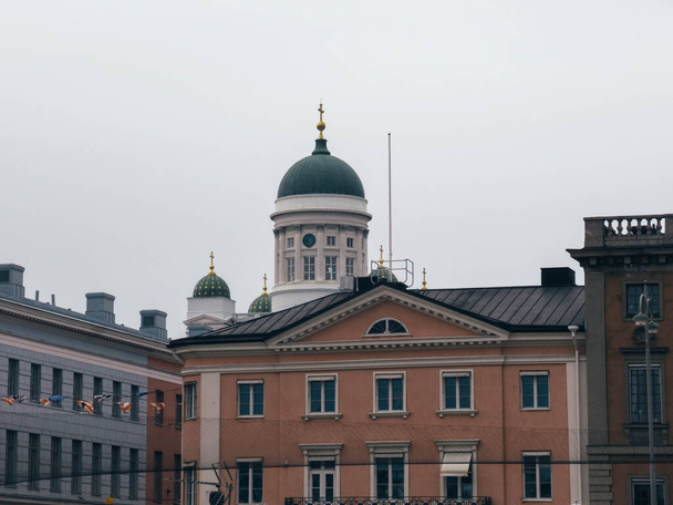 Helsingin katedraali värikkäiden rakennusten takana pilvisenä päivänä. - Valokuva, kuva