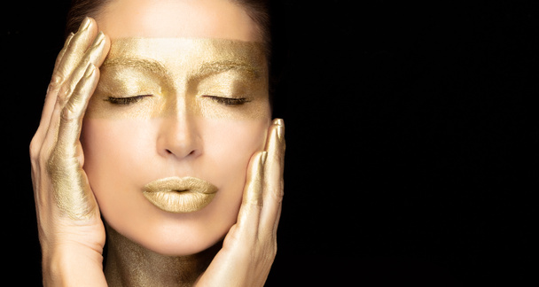 Beautiful woman half face with glowing golden skin, eyes closed and a serene expression. 24k gold based spa skincare treatment concept. Close up beauty portrait isolated on black - 写真・画像