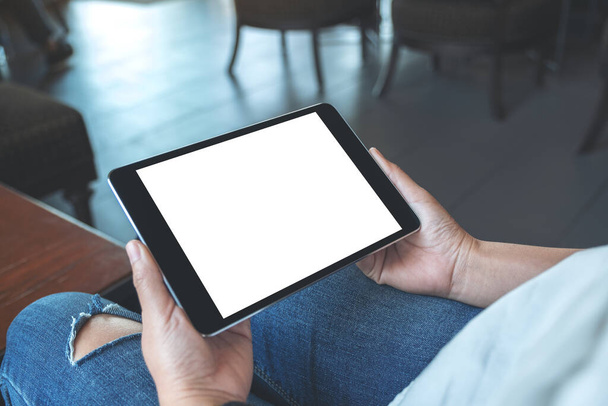 Mockup image of a woman sitting and holding black tablet pc with blank white desktop screen horizontally - Foto, Imagem