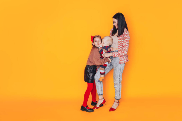 Mom with children in front of a yellow background. A happy family without a father. Mom holding a small child. - Foto, imagen