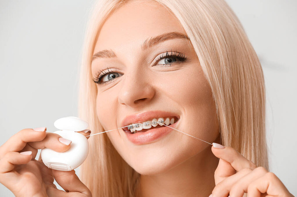 Mujer joven con aparatos dentales y hilo dental sobre fondo claro - Foto, imagen