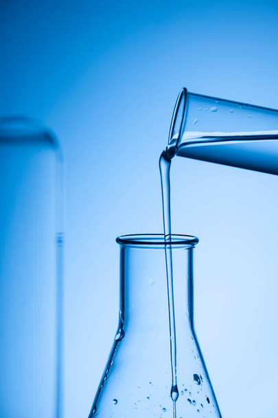 Filling an Erlenmeyer flask from a test tube against a blue-toned studio background. - Fotoğraf, Görsel