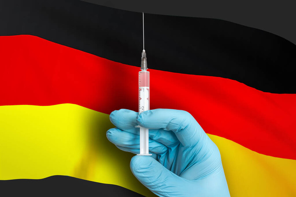 Прививка в Германии. Вакцина для защиты от Ковид-19 на фоне национального флага. - Фото, изображение