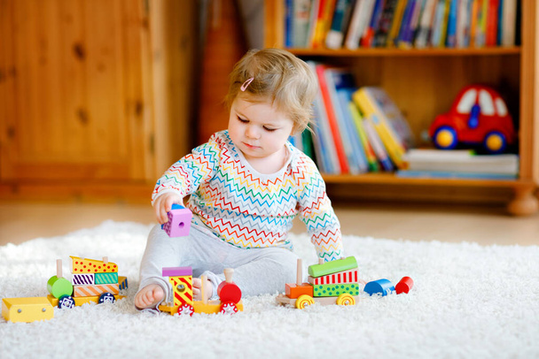 kleines Mädchen, das zu Hause oder im Kinderzimmer mit pädagogischem Holzspielzeug spielt. Kleinkind mit bunter Schleppe. Kinder haben Spaß mit verschiedenen Spielzeugen. Einsames Kind während Coronavirus-Pandemie in Quarantäne - Foto, Bild