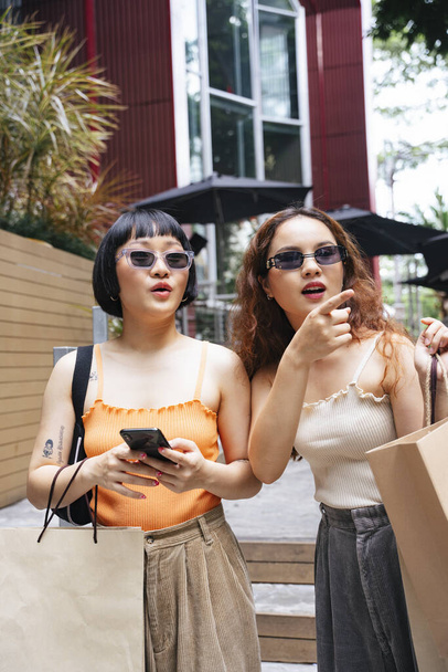 Portret dwóch młodych azjatyckich kobiet nosi okulary przeciwsłoneczne w poszukiwaniu sklepu w centrum handlowym. - Zdjęcie, obraz